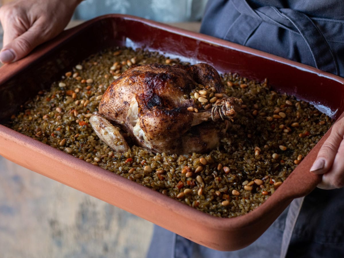 Chicken stuffed with freekeh in a baking tray held by a woman in an apron
