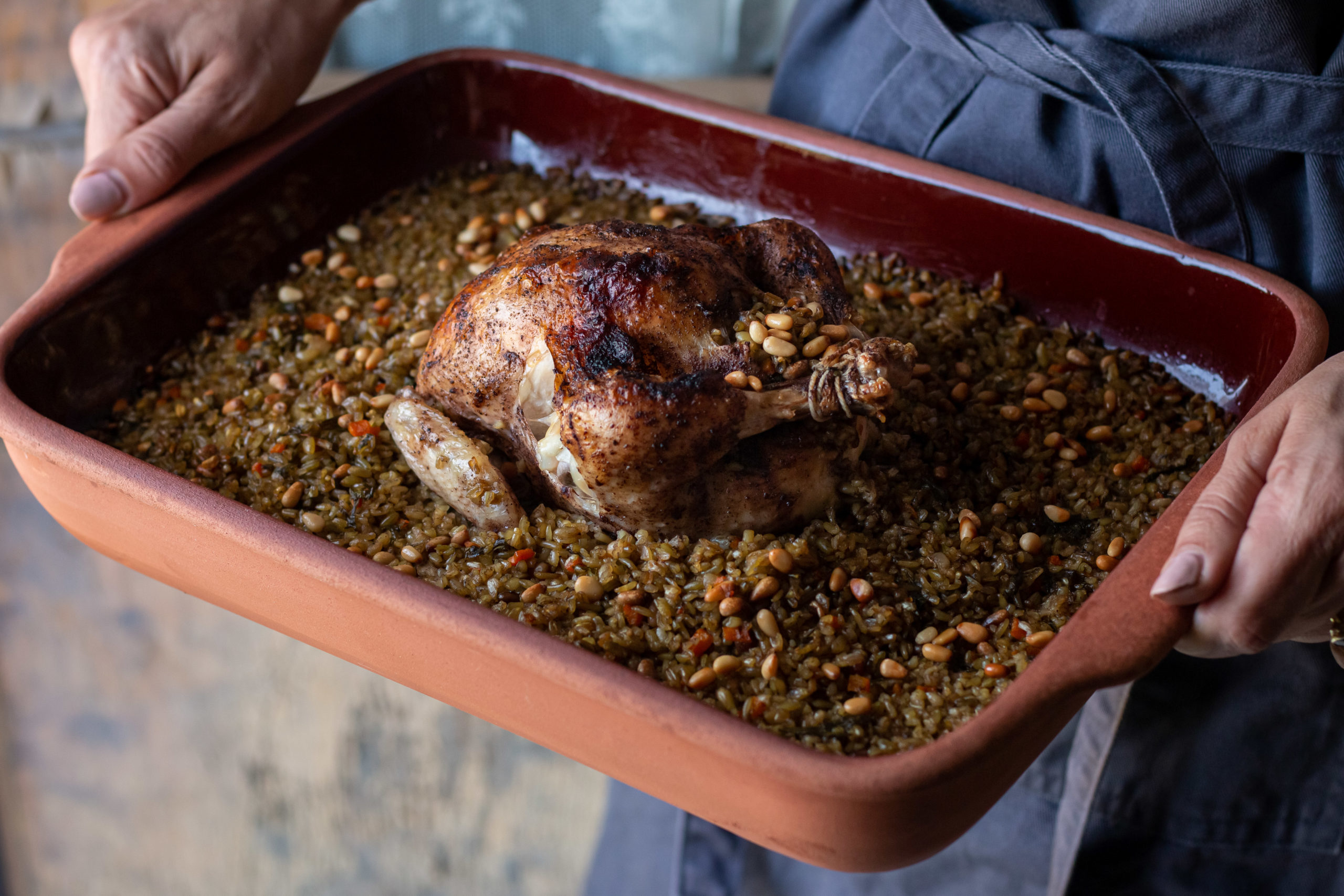 Chicken stuffed with freekeh in a baking tray held by a woman in an apron