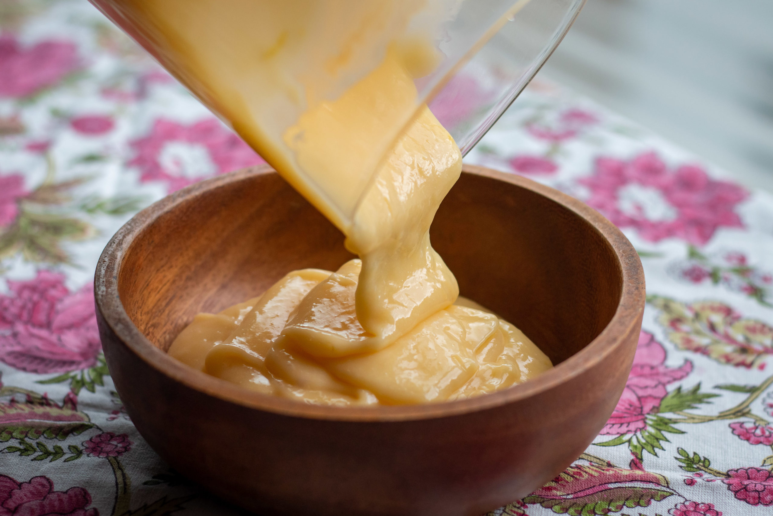 Lime curd being poured from a plastic container to a wooden bowl