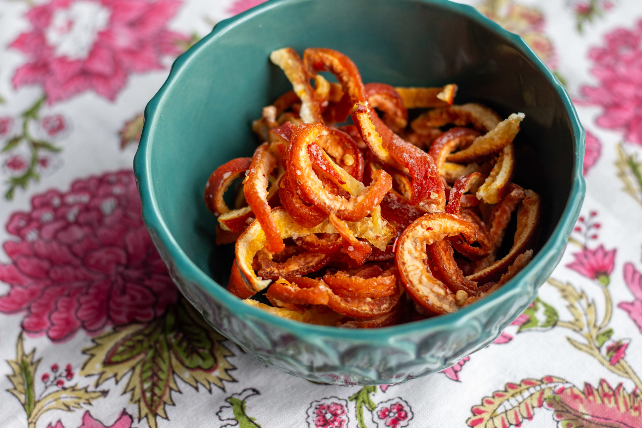Candied citrus peel in a teal ceramic bowl on a floral tablecloth