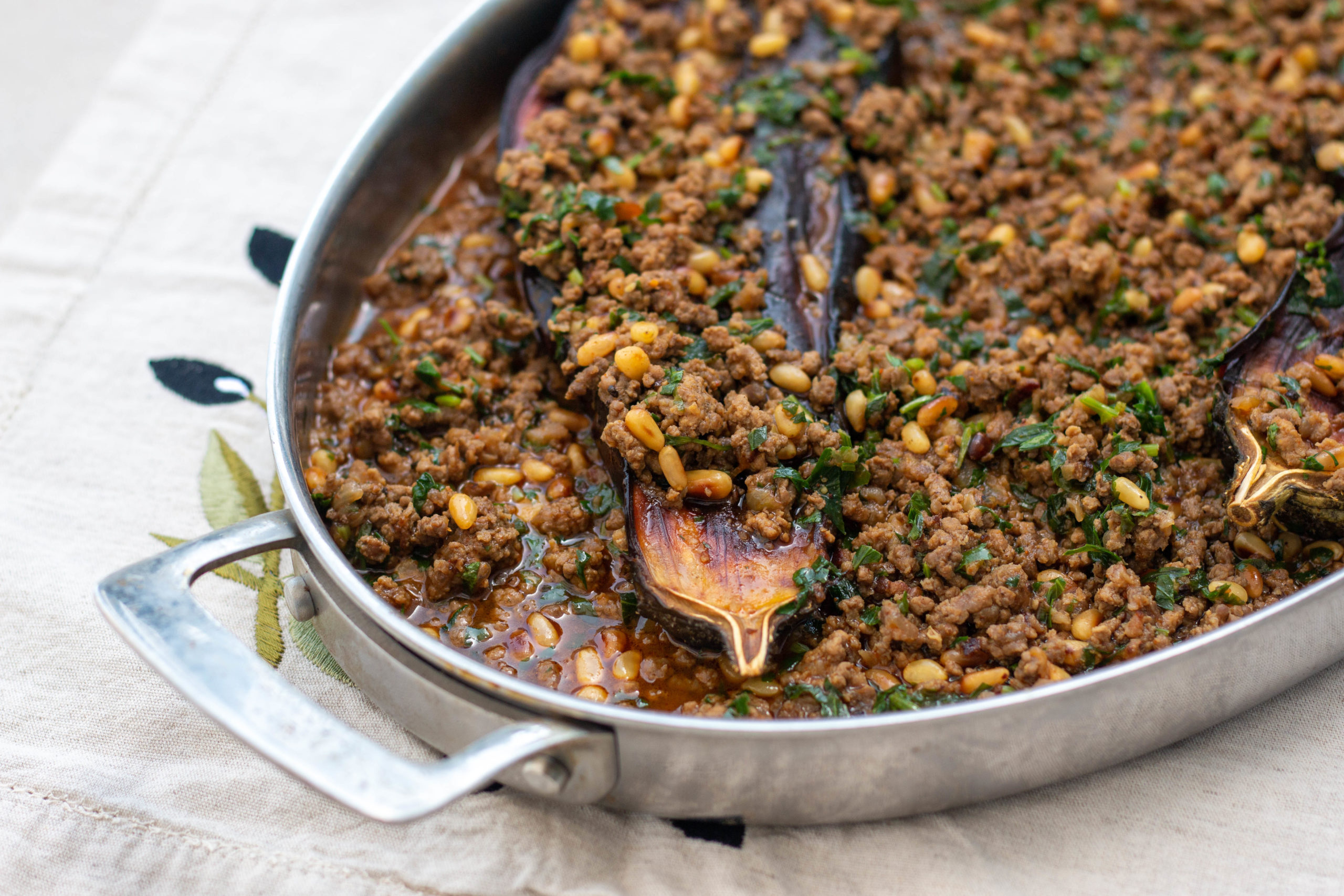 Oval casserole dish with eggplant, ground meat, pine nuts and herbs on a white tablecloth