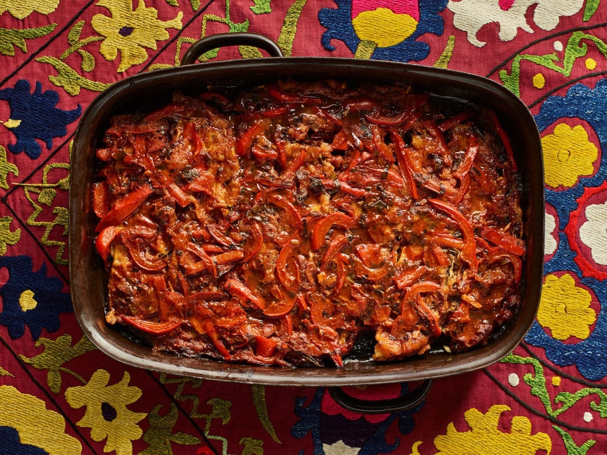 Eggplants with tomatoes and peppers in a rectangular baking dish atop a colorful tablecloth