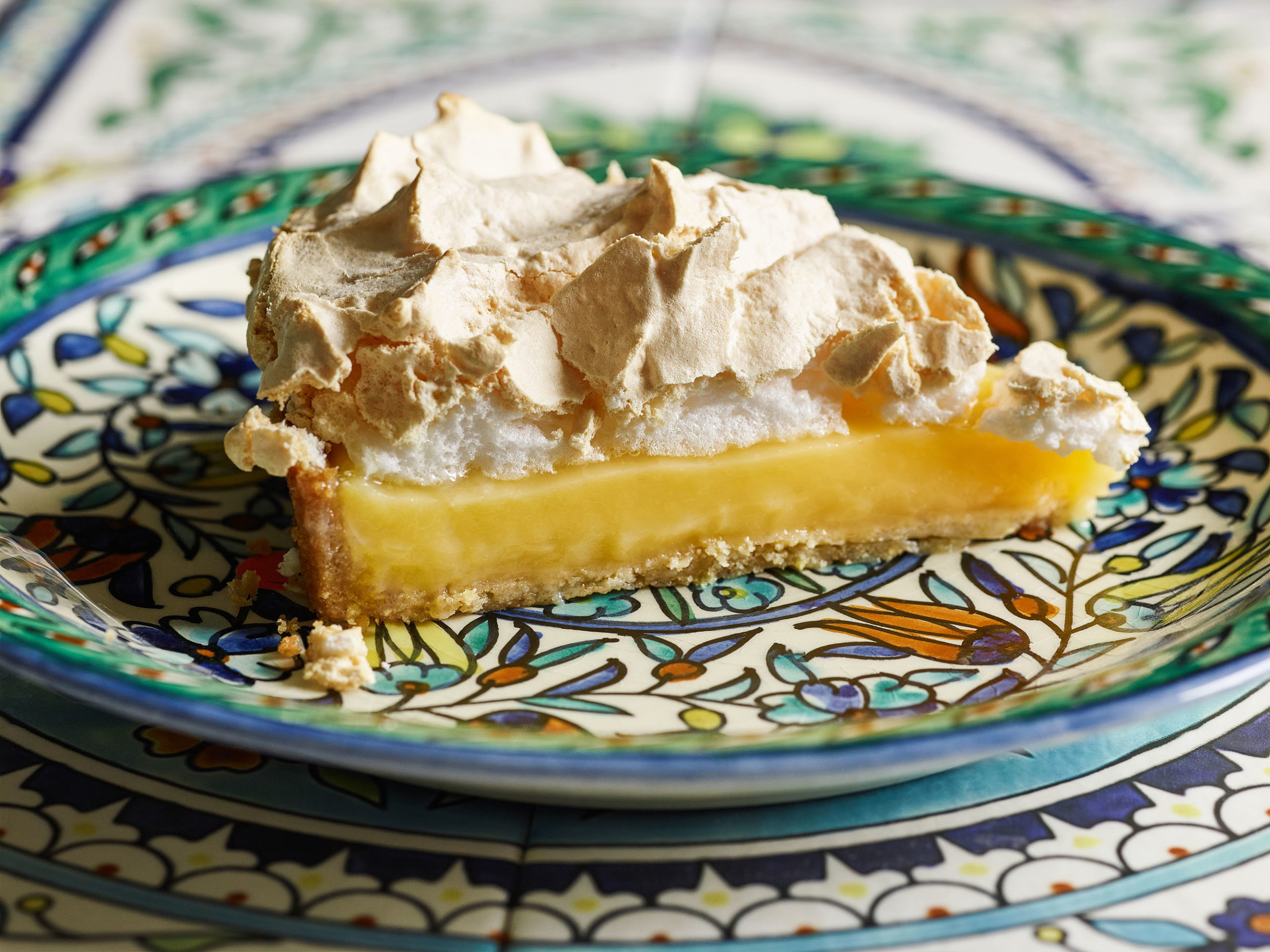 Slice of lemon meringue pie on a ceramic plate with blue dtail