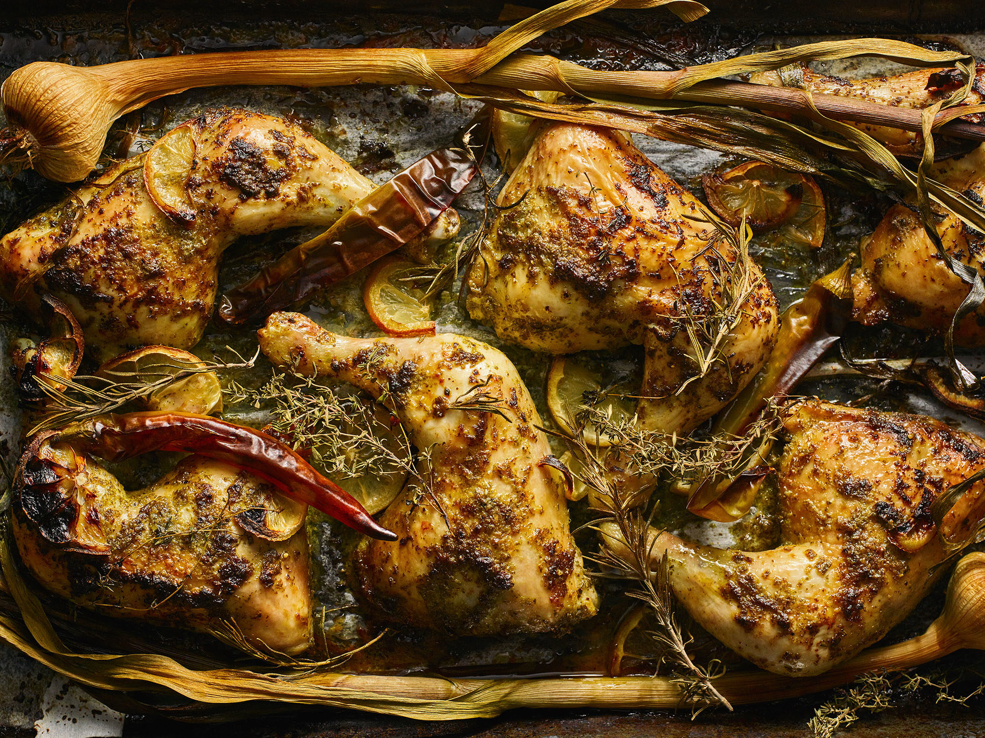 Roast chicken legs with chili peppers and herbs on a baking tray