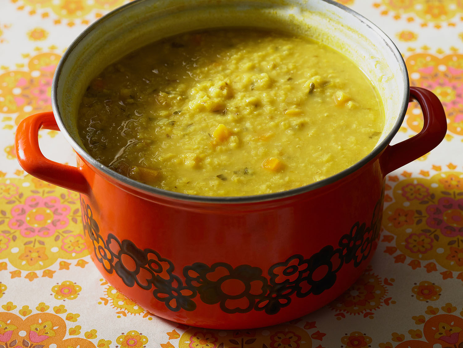 Arab lentil soup in a vintage orange pot atop a flowered tablecloth