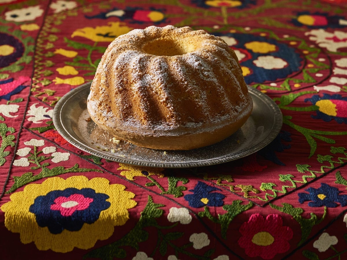 Orange juice bundt cake on a silver platter atop a colorful red tablelcoth