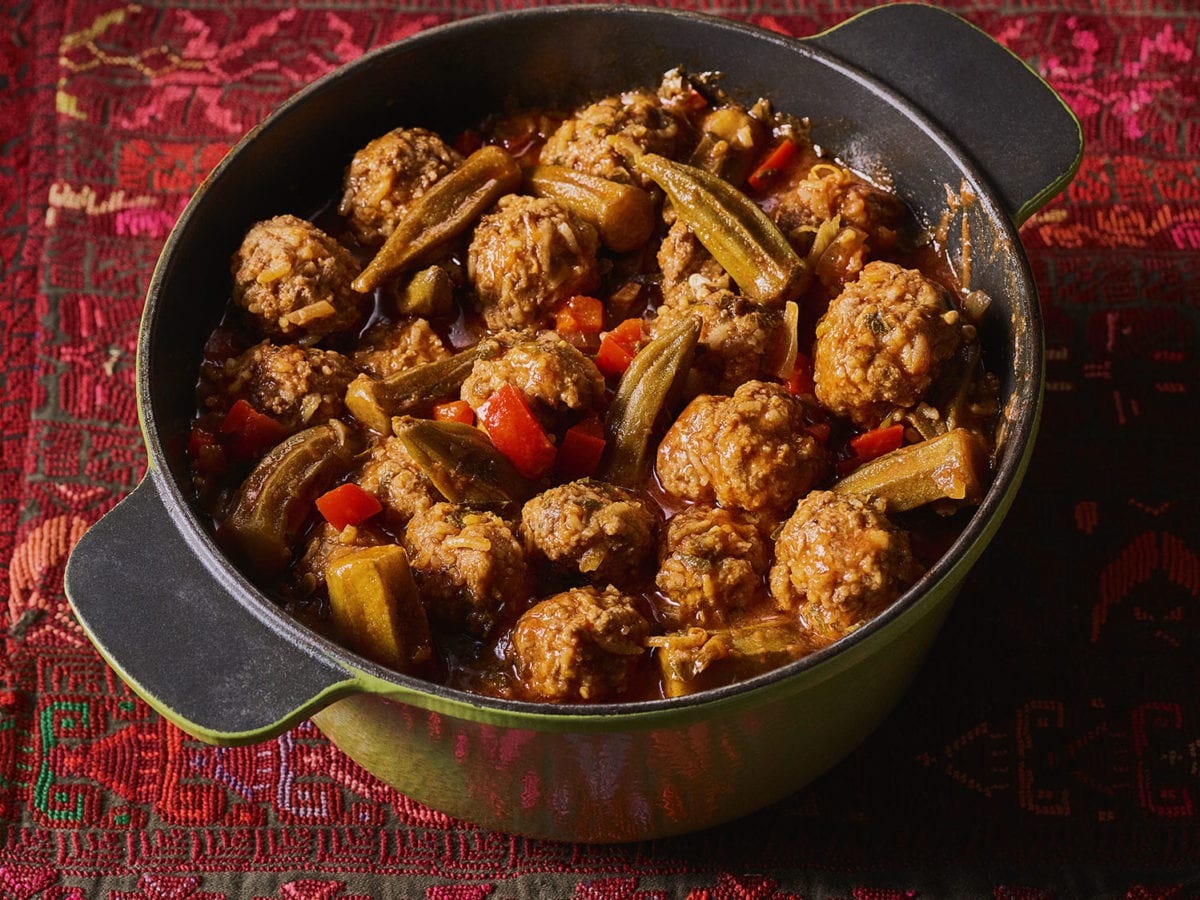 Meatballs with okra in a green Dutch oven atop a red tablecloth