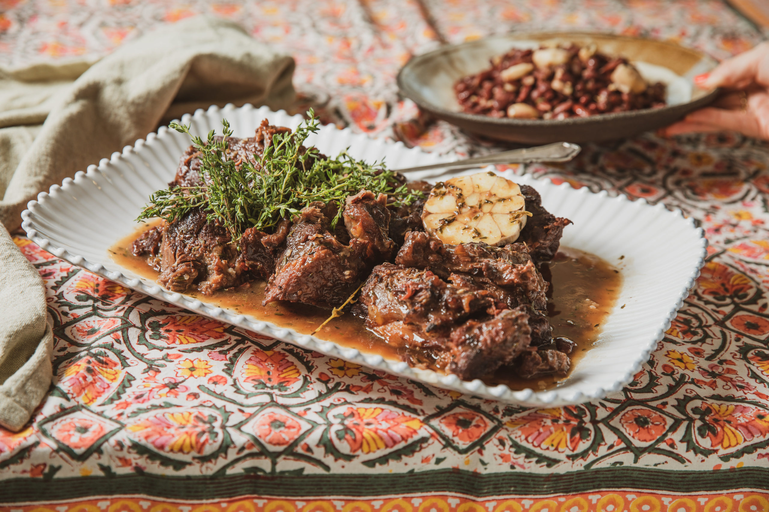 A platter of beef cheek stew and a bowl of kidney beans atop a colorful tablecloth