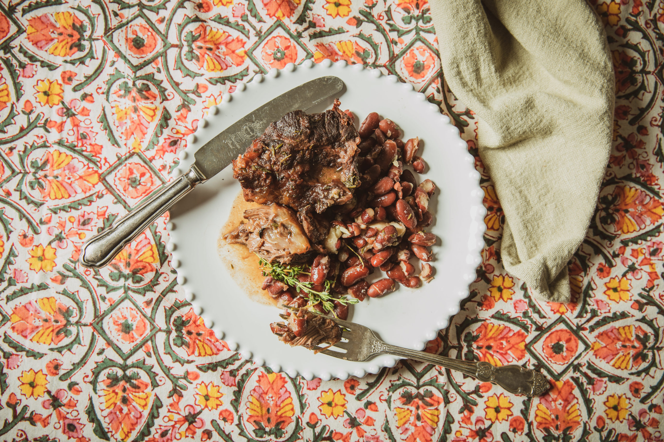 Beef cheek stew with kidney beans on a white plate atop a colorful tablecloth
