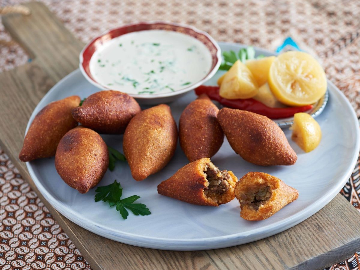 Persian fried kibbeh on a blue plate with a bowl of sauce and lemons