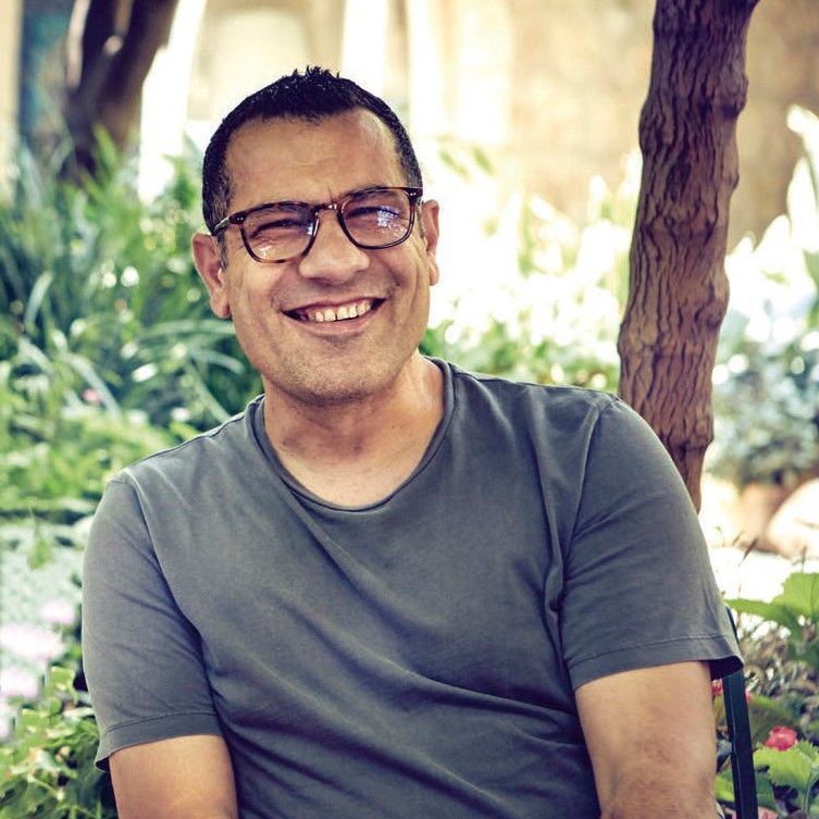 Portrait of author Sami Tamimi wearing a gray shirt and glasses