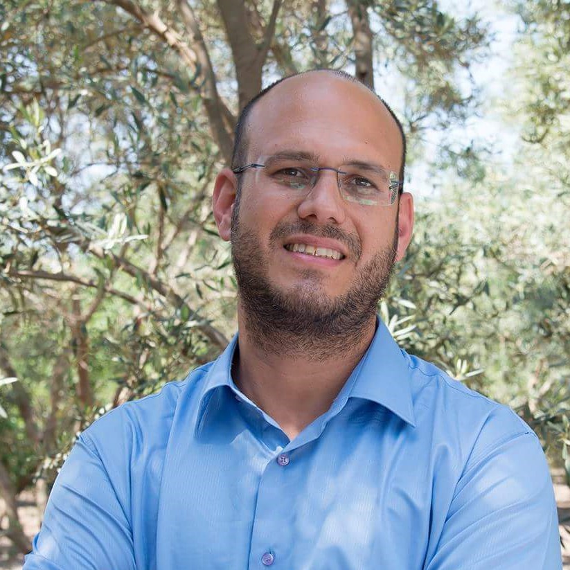 Man in blue shirt standing infront of an olive tree