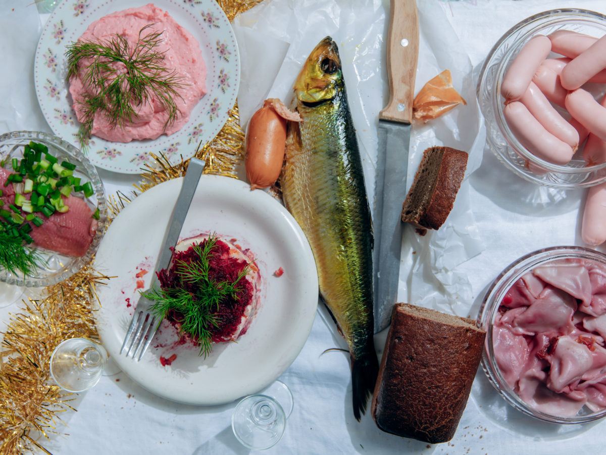 Plates of Russian dishes like cured meats and fish atop a white tablecloth