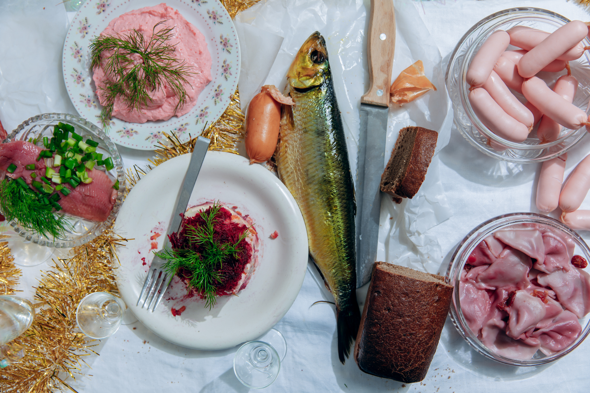 Plates of Russian dishes like cured meats and fish atop a white tablecloth