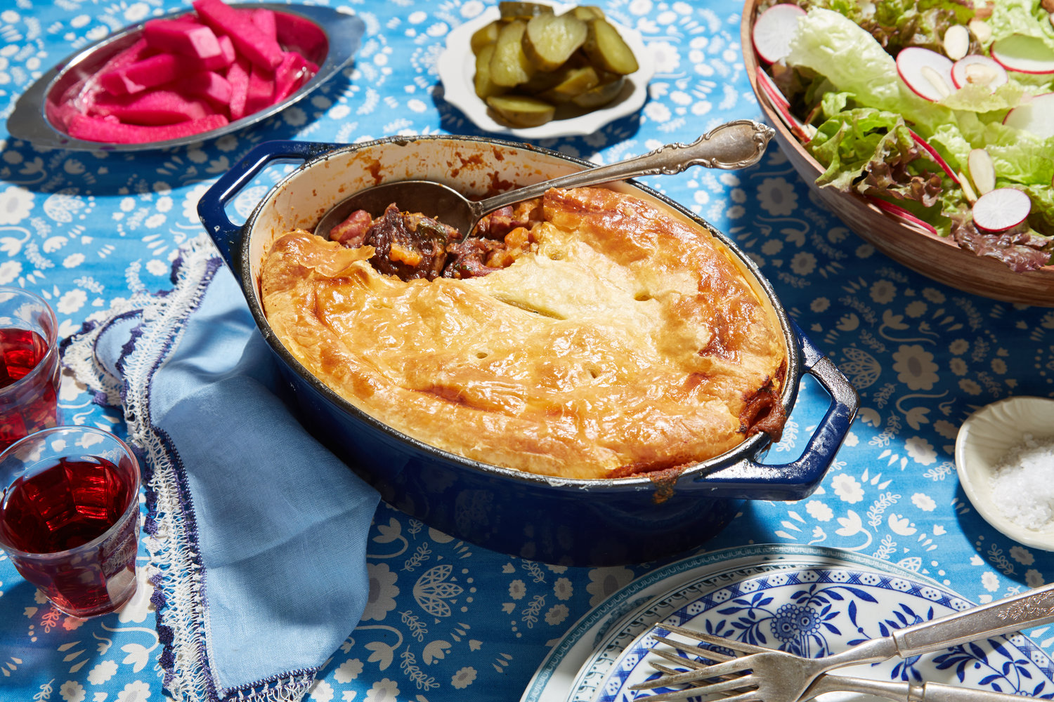 Blue casserole dish with cholent pot pie and a large serving spoon