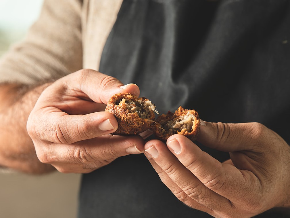 Two hands holding a meat-filled fritter called kibbeh haleb