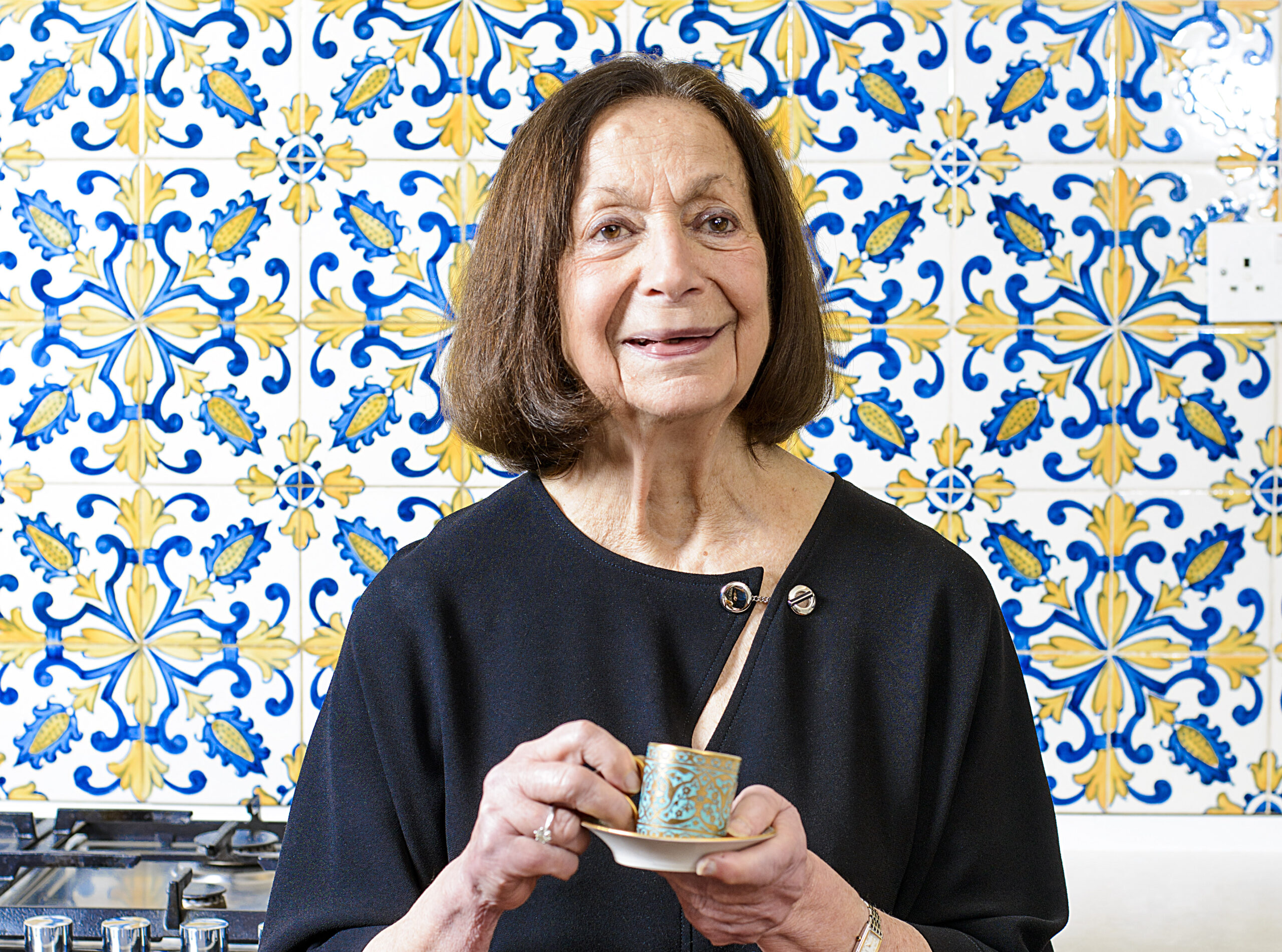 Cookbook author Claudia Roden infront of a wall of decorative kitchen tiles