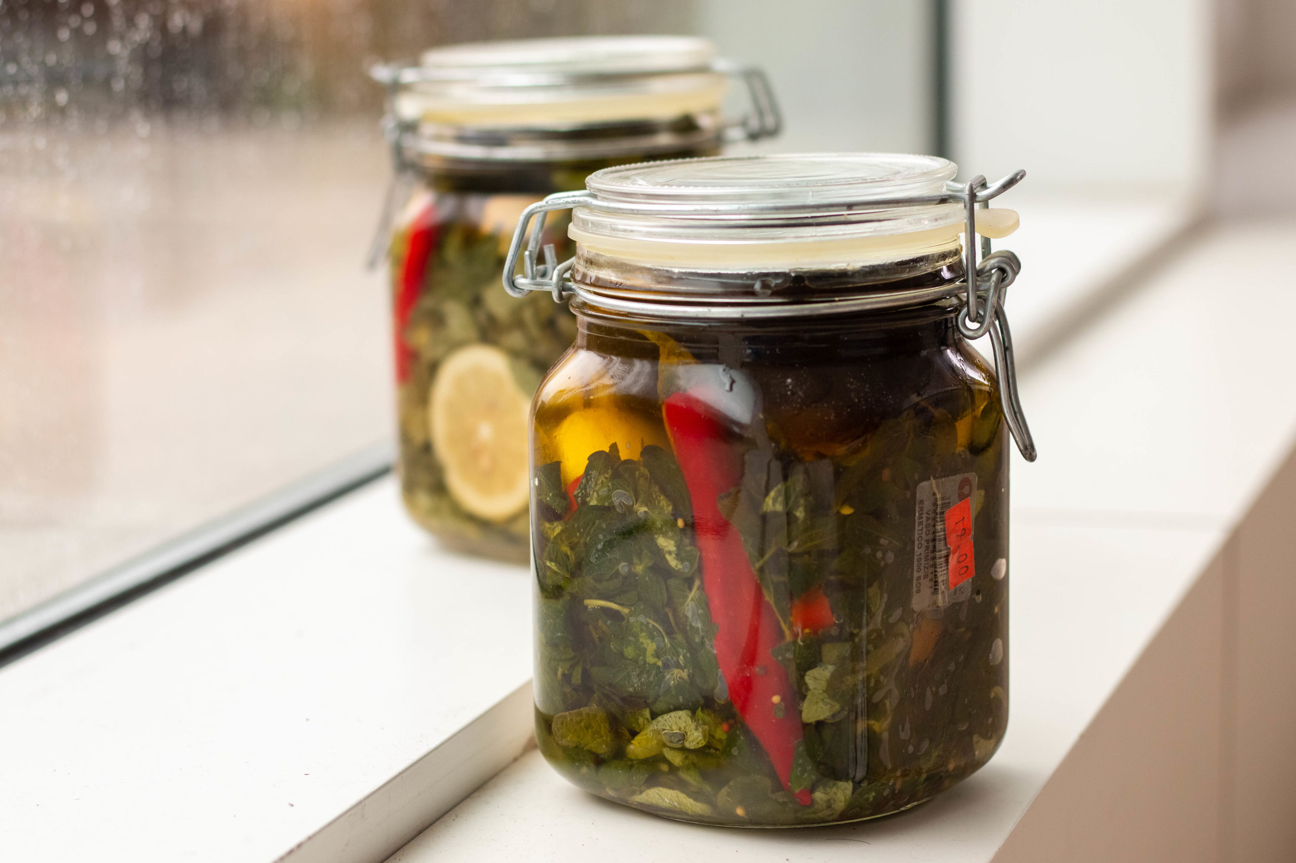 Glass jars with fresh za'atar leaves curing in oil with spices