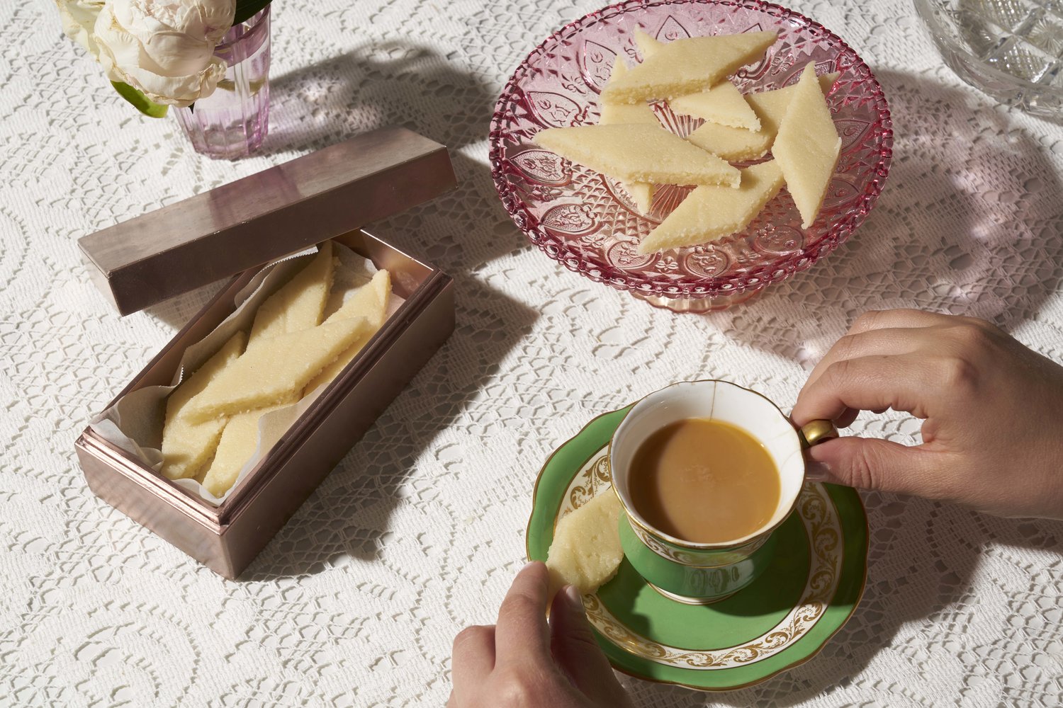 Slices of marzipan on a pink glass plate alongside small cup of tea