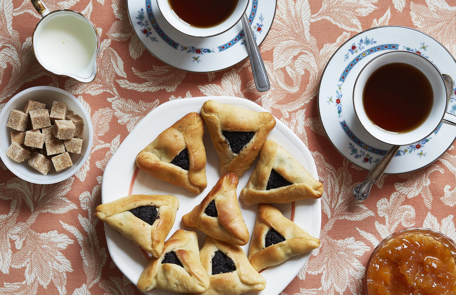 White plate of hamantaschen cookies next to cups of tea