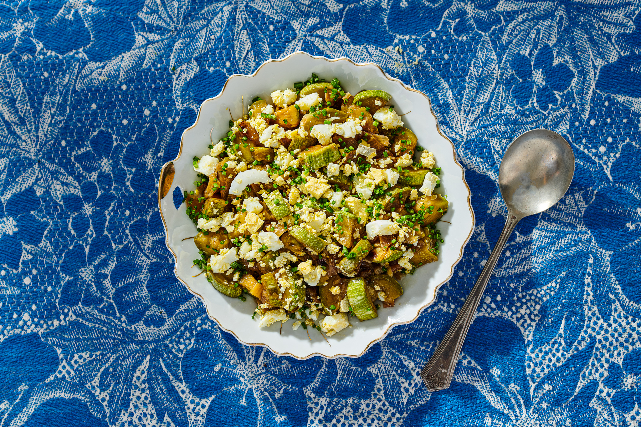 White bowl with zucchini and egg salad on blue tablecloth