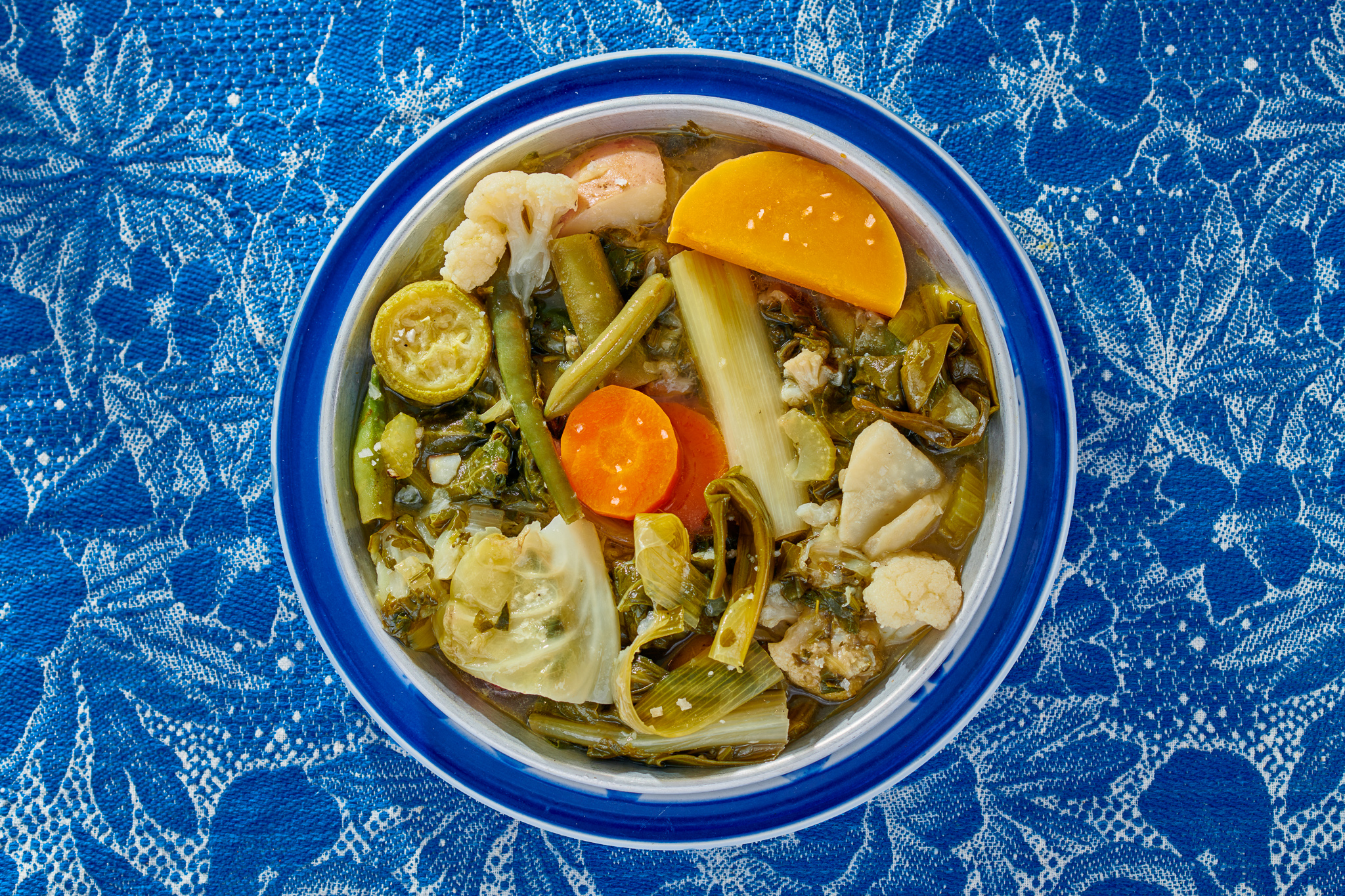 Vegetables in broth in blue bowl on blue tablecloth