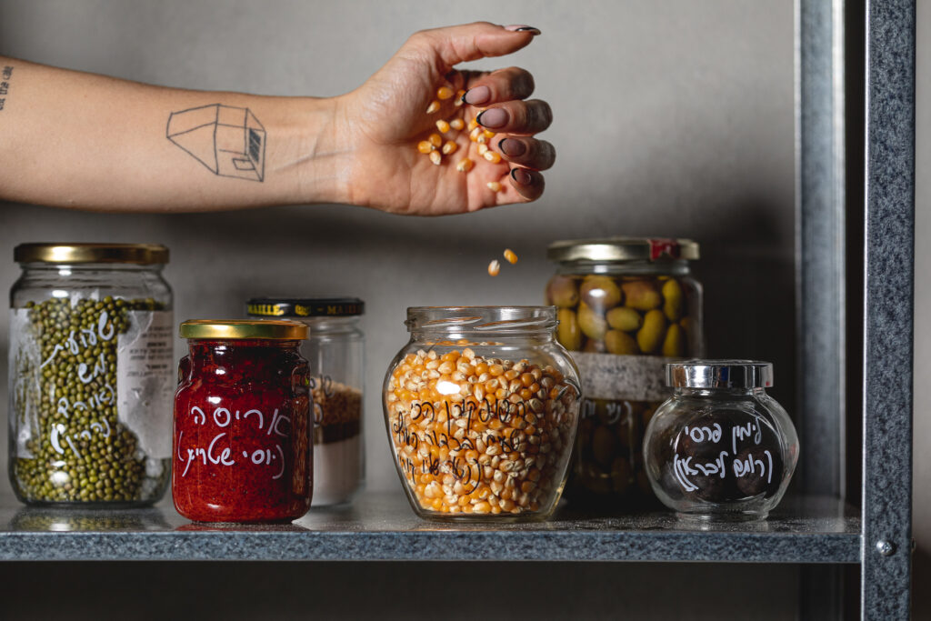 Jars of pantry items on a shelf with a hand holding popcorn kernels
