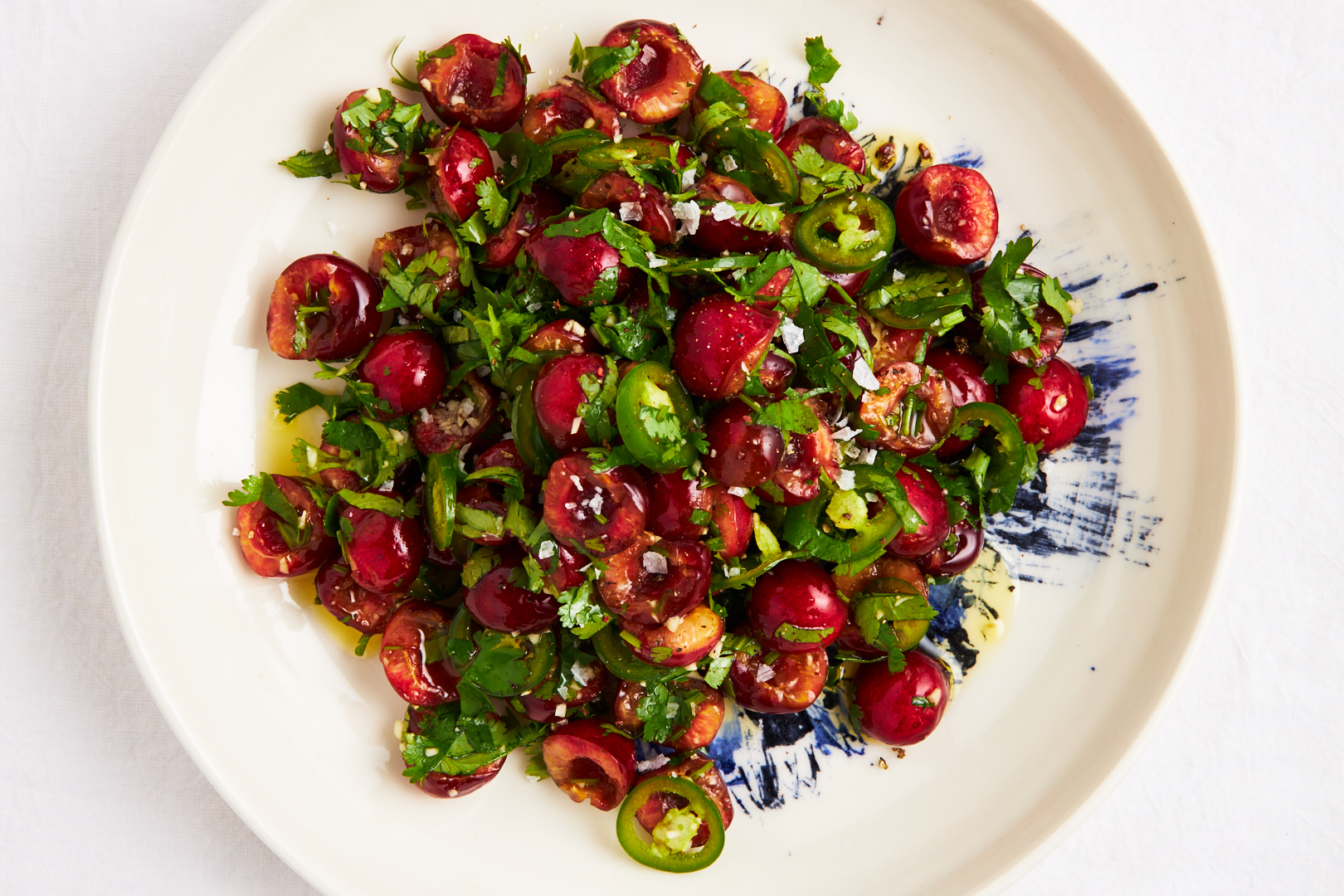 Cherry salad with chili and cilantro atop a white plate and white background