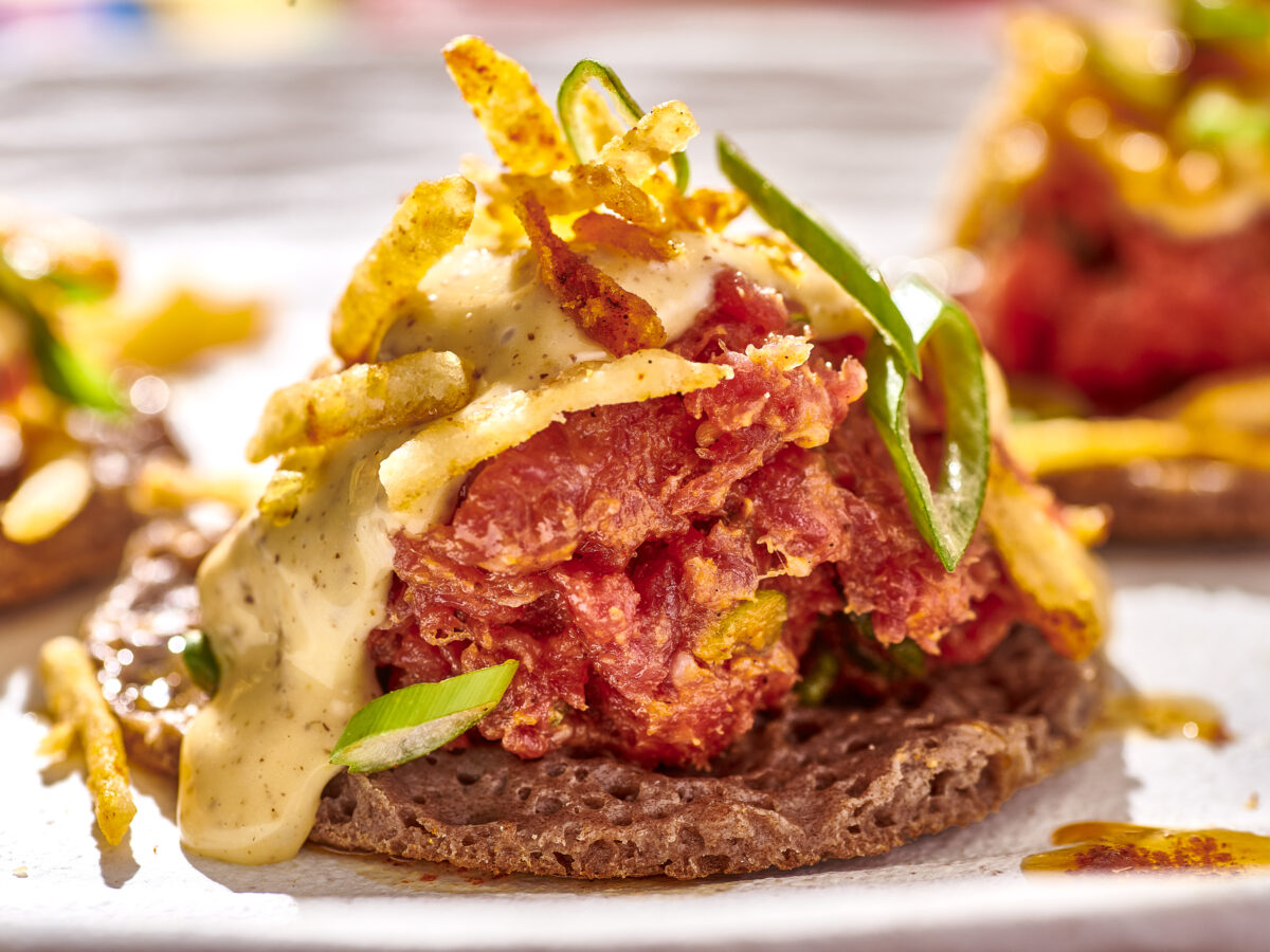 Ethiopian steak tartare finished with sauce and potato chips sits atop small injera