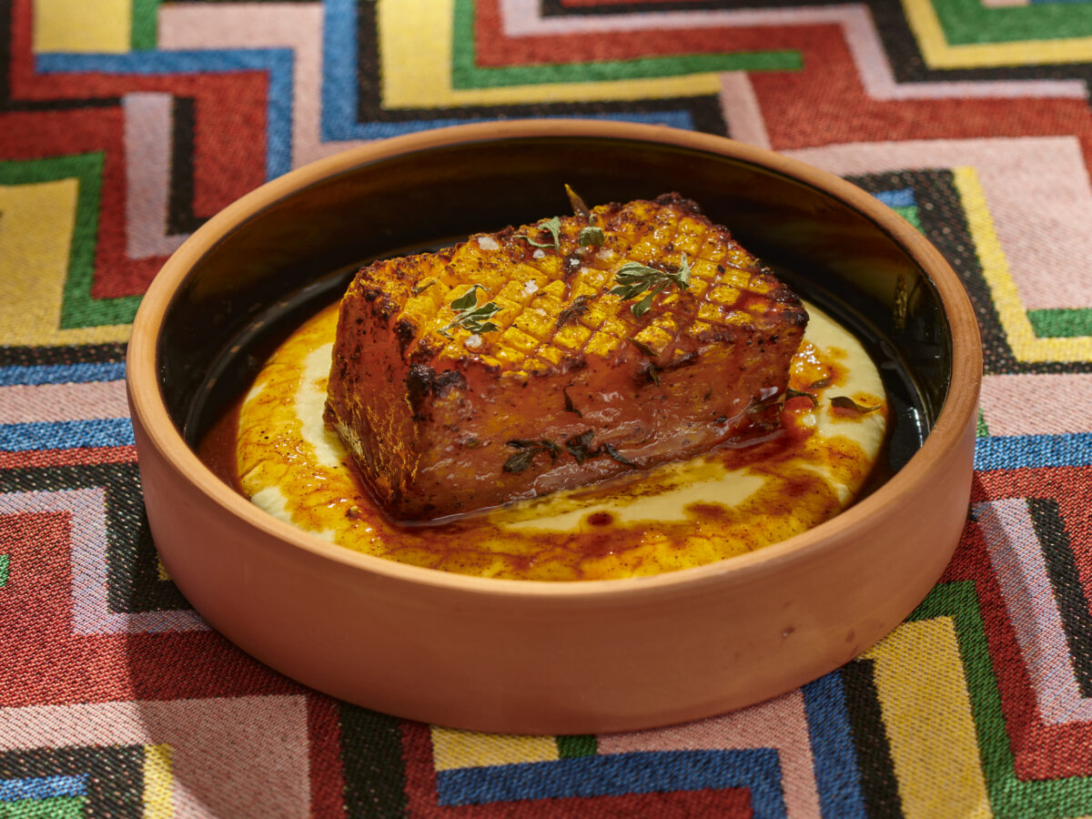 Pumpkin steak and yellow split pea puree sit in a terracotta bowl with a black interior