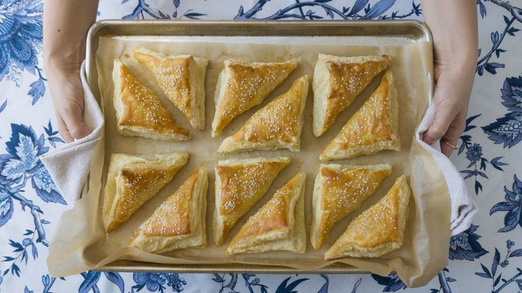 Baking tray with triangular puff pastries are presented atop a white and blue tablecloth