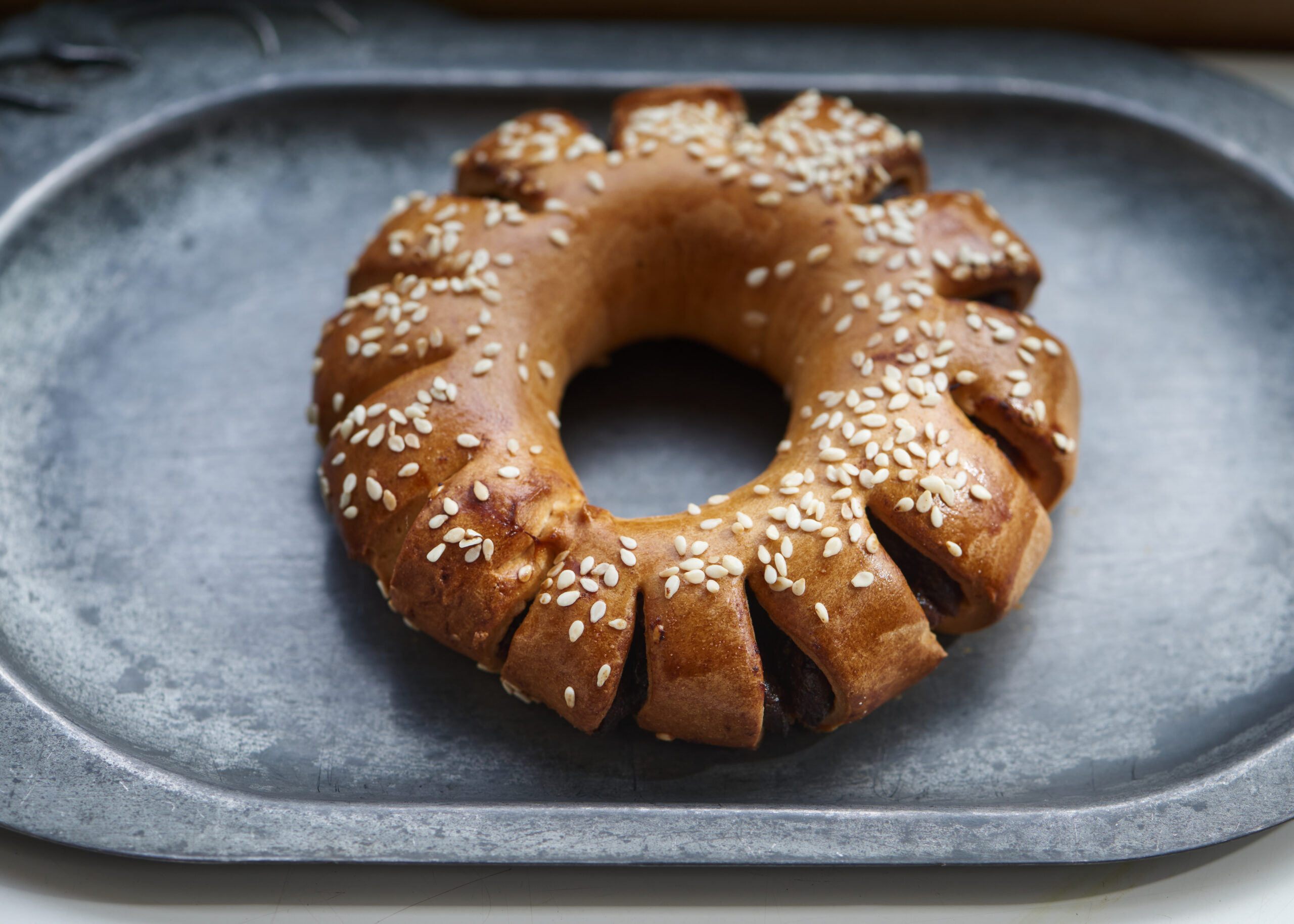 Ring-shaped pastry with sesame seeds on gray tray