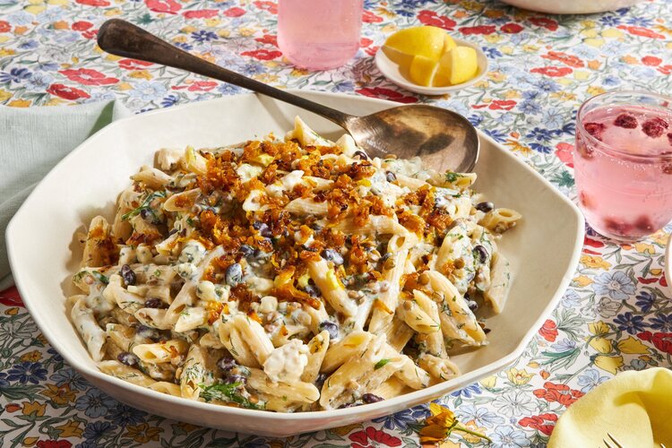 Large white bowl of pasta with yogurt and beans is placed on a colorful floral tablecloth