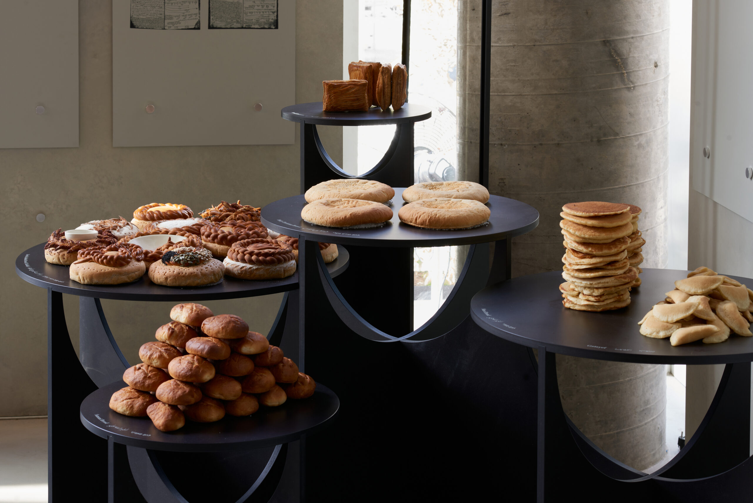 Black tables with various breads in a gallery space with natural light