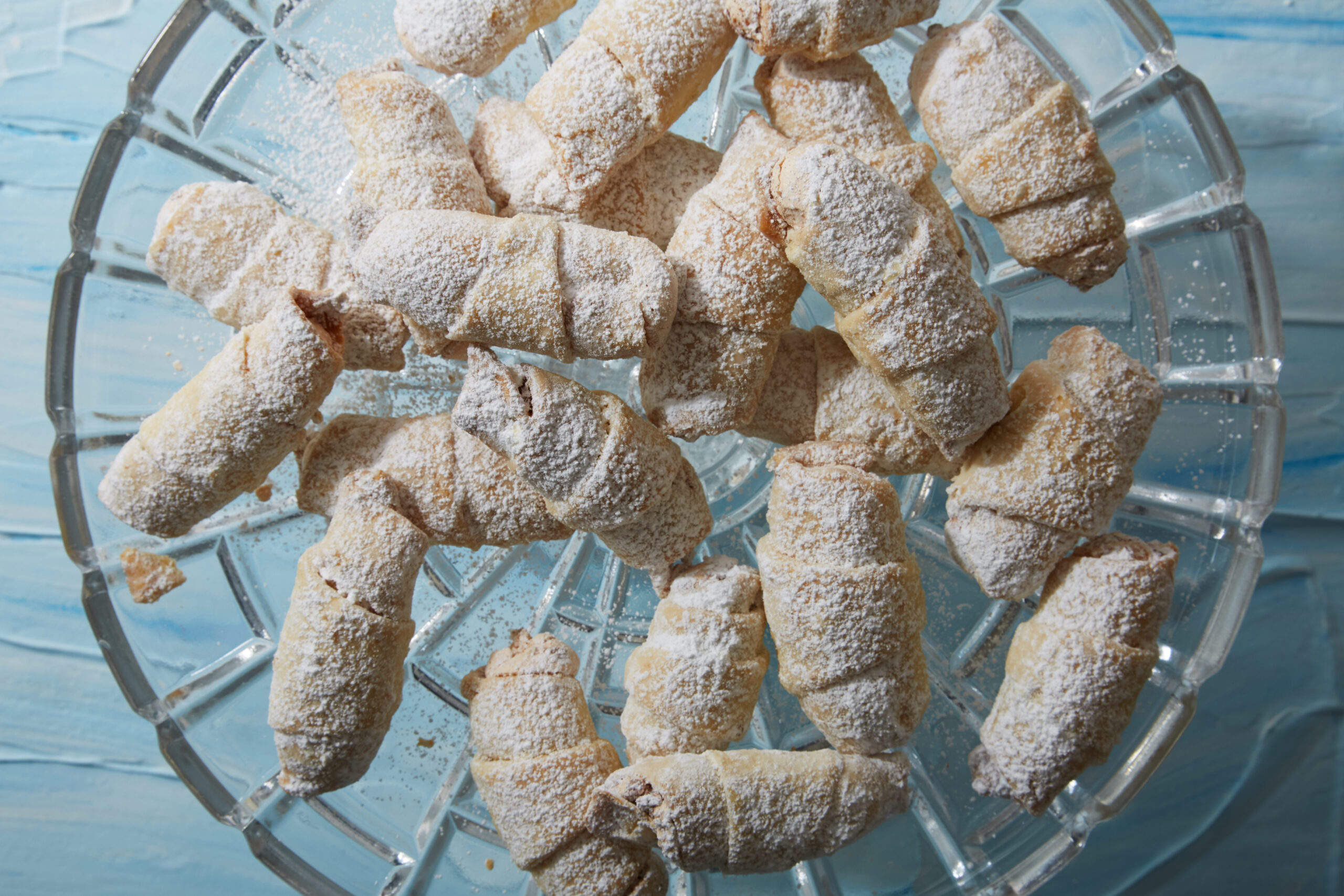 Small rugelach pastries dusted with powdered sugar on glass tray
