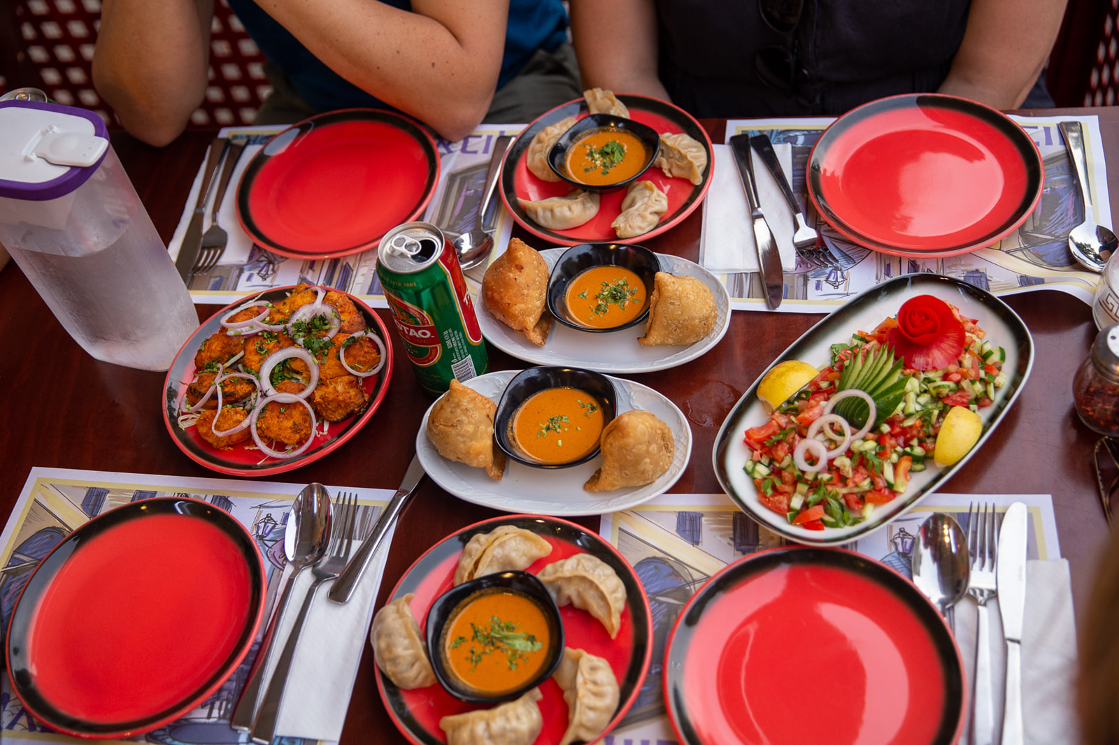 Colorful table with red plates, samosas, dumplings, and salads