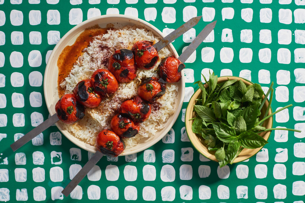 Tomatoes on skewers over rice with bowl of herbs