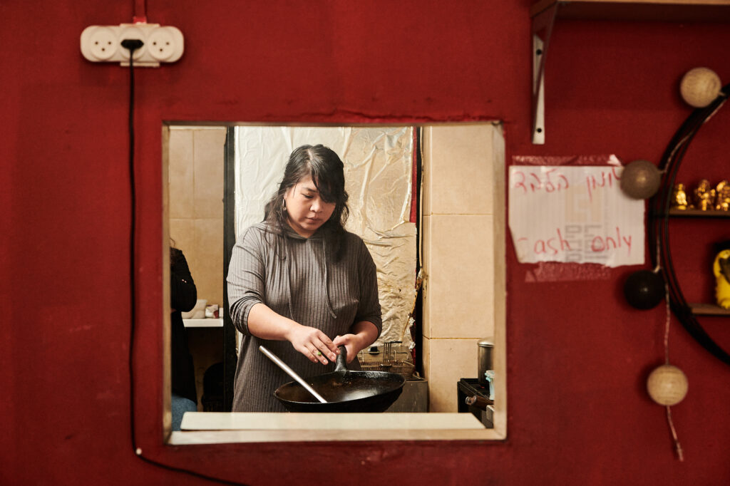 Woman cooking with wok through small kitchen window