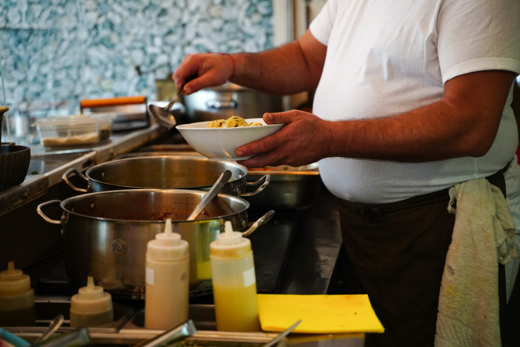 Man in white shirt serving food from large metal pots