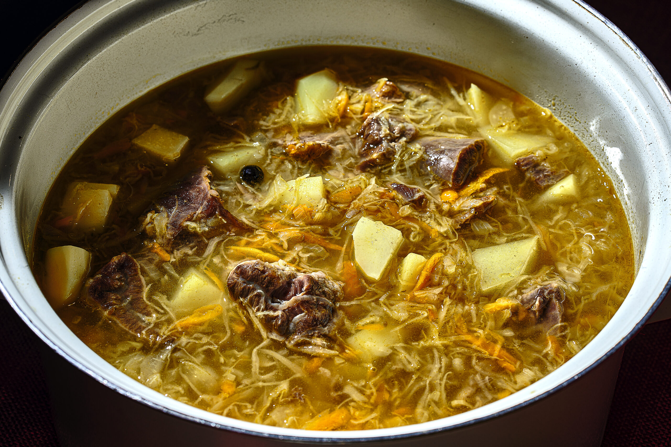 Enamel pot of Russian cabbage soup with potato and meat chunks