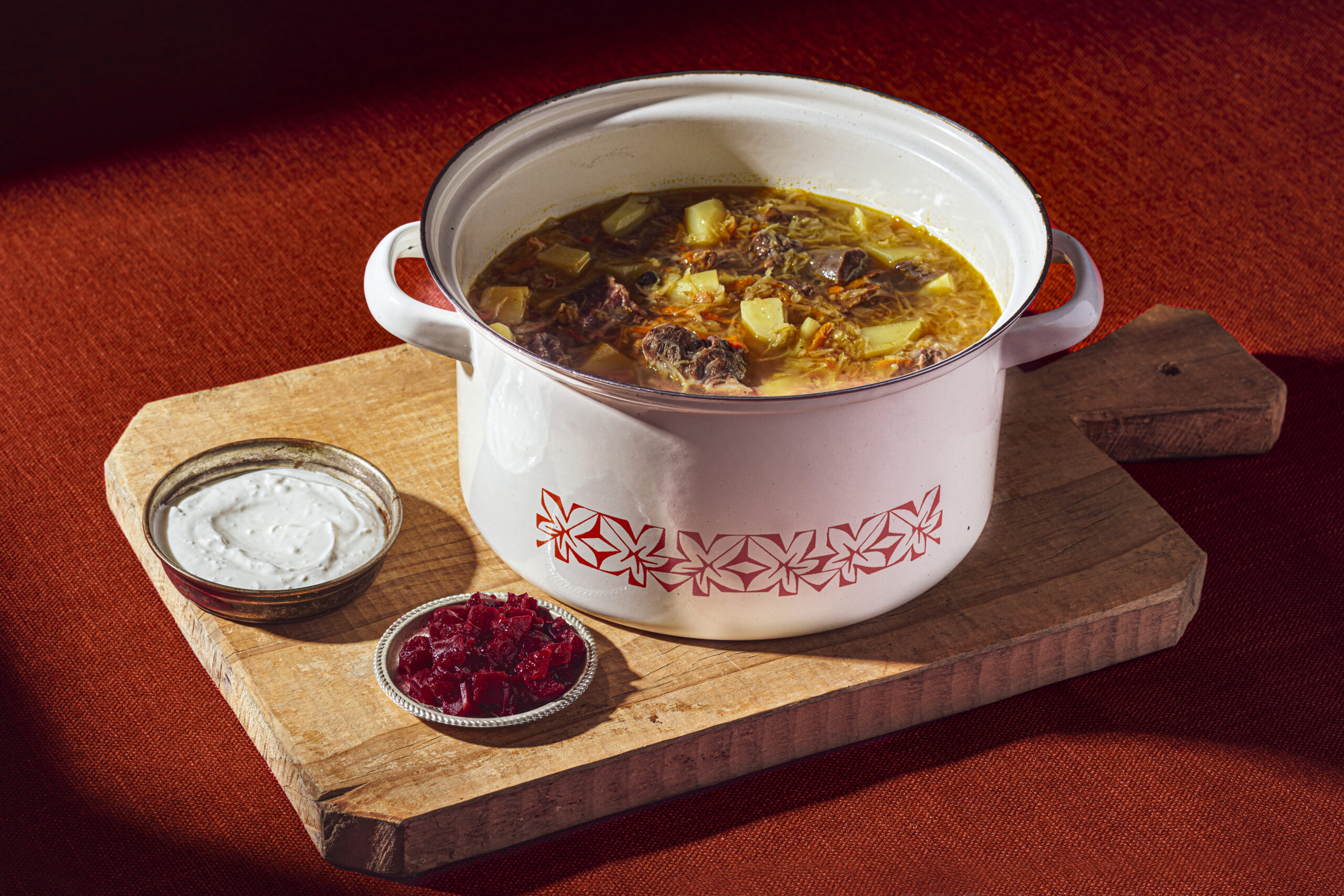 Russian cabbage soup in white enamel pot on top of wooden cutting board