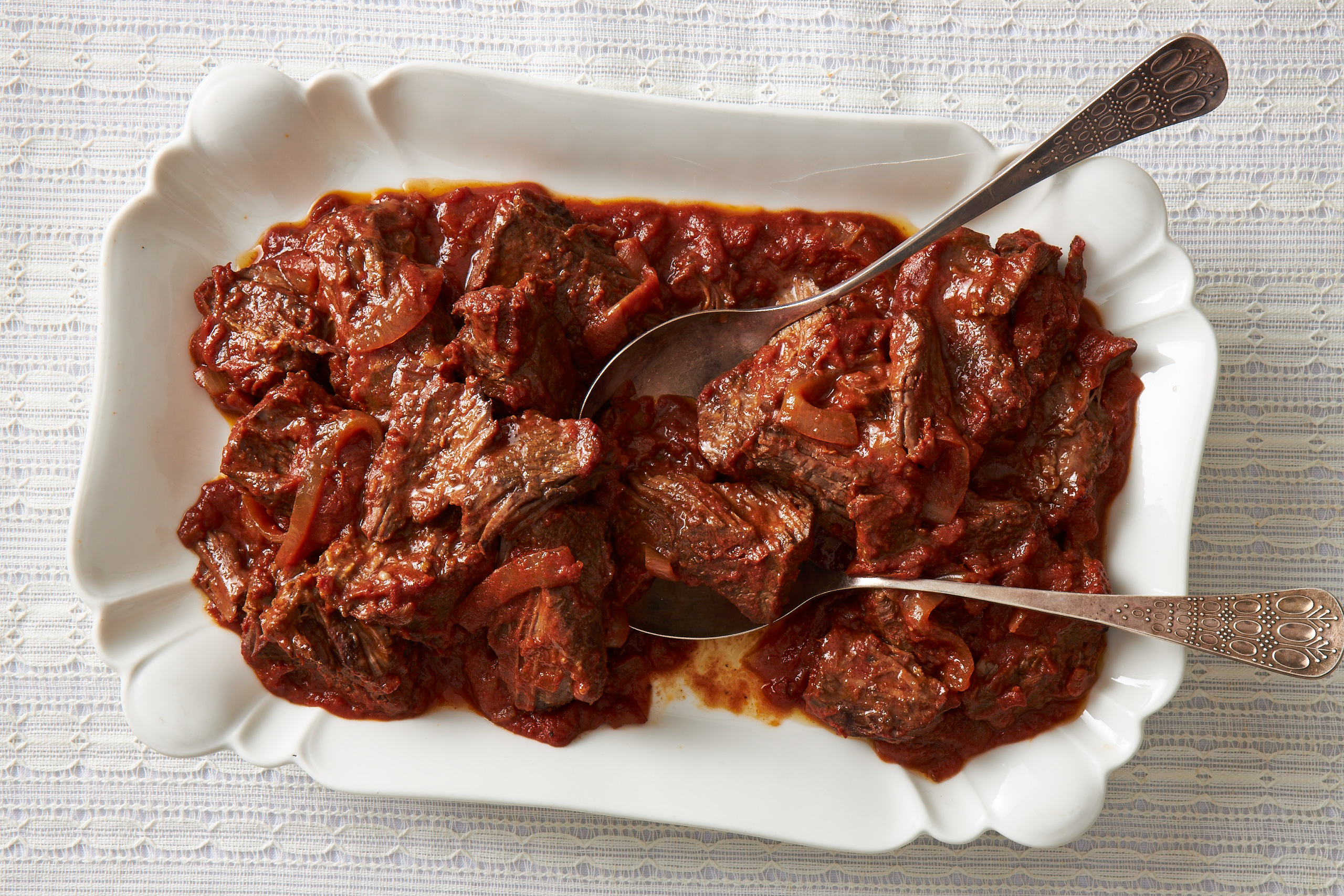 Chunks of beef in tomato sauce on white rectangular plate