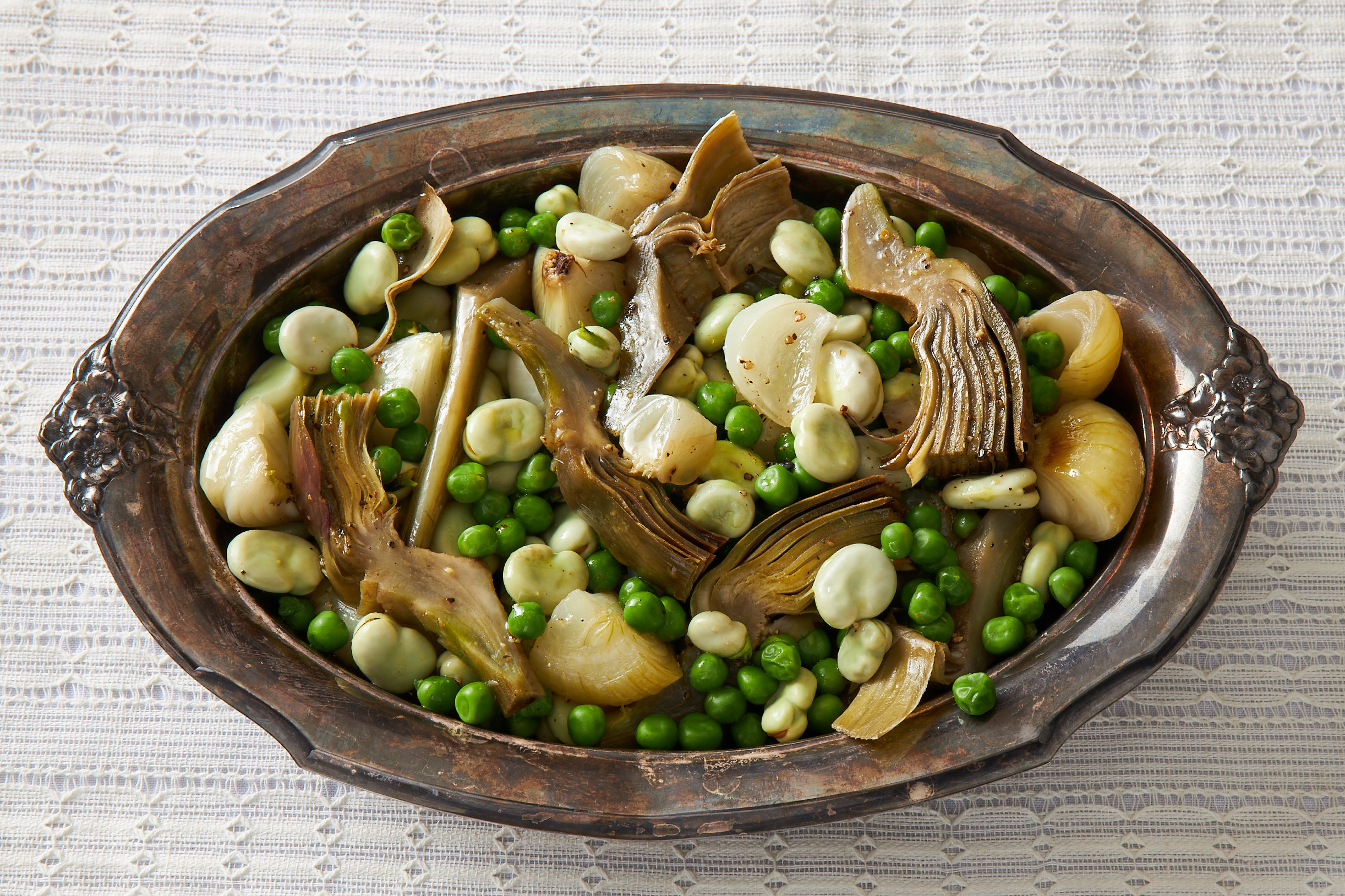Braised artichokes, peas, fava beans and onions in metal bowl