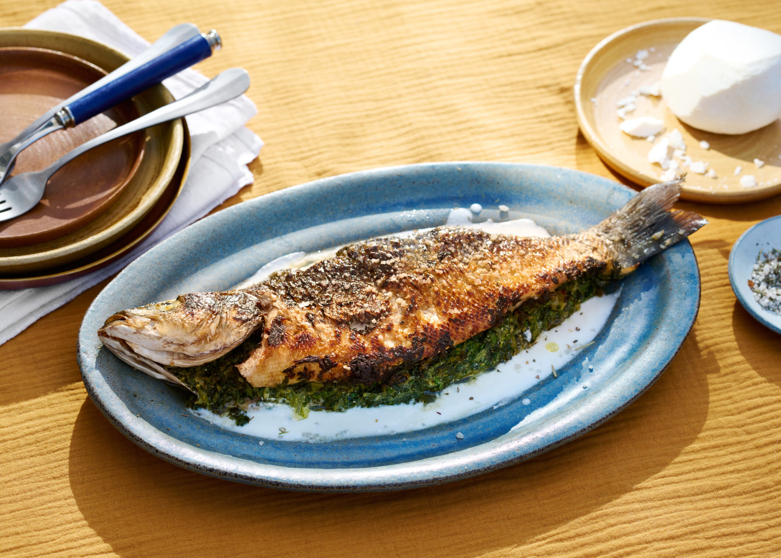 Whole roasted fish stuffed with herbs served on blue plate with yogurt sauce