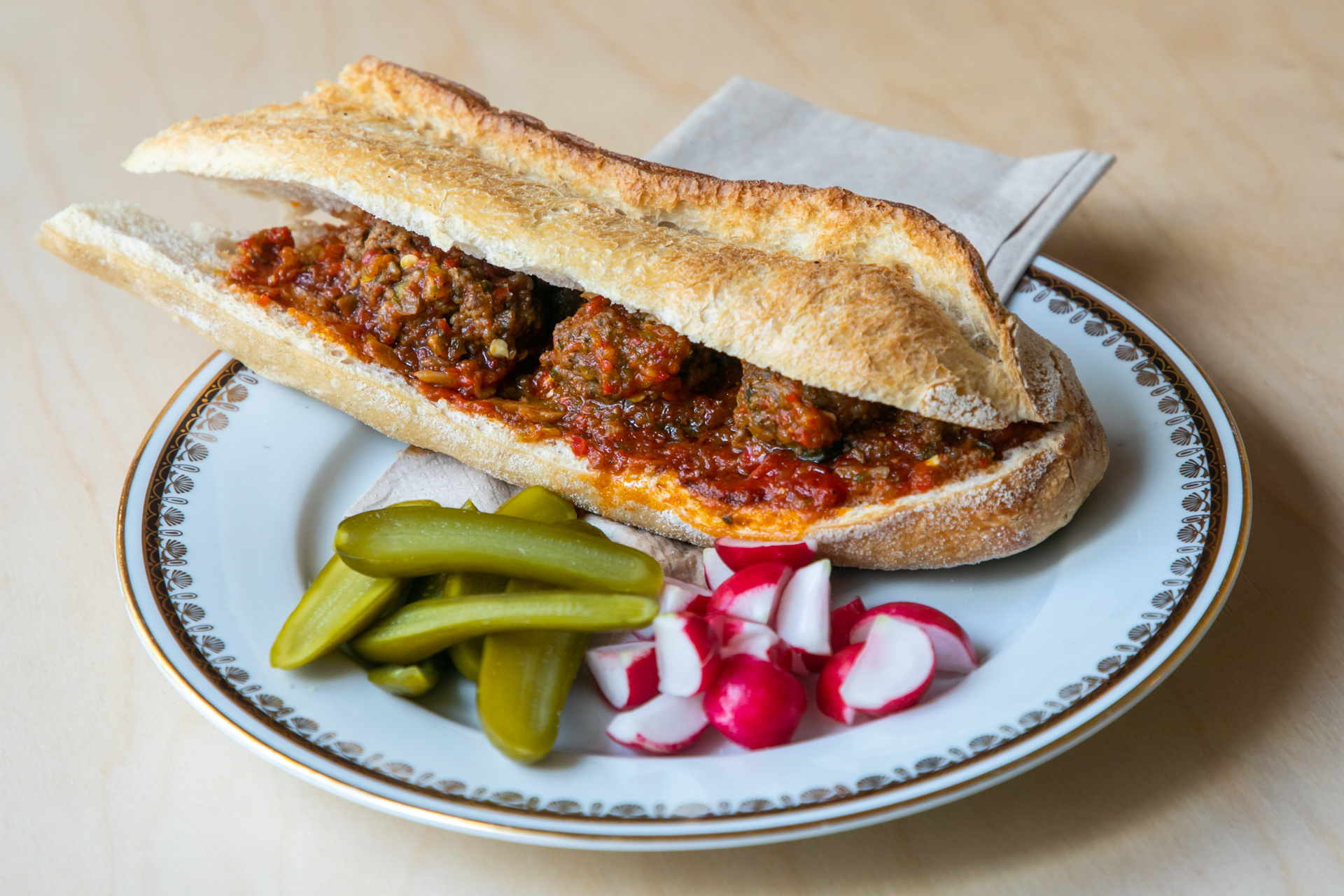 Baguette sandwich with meatballs alongside radishes and pickles