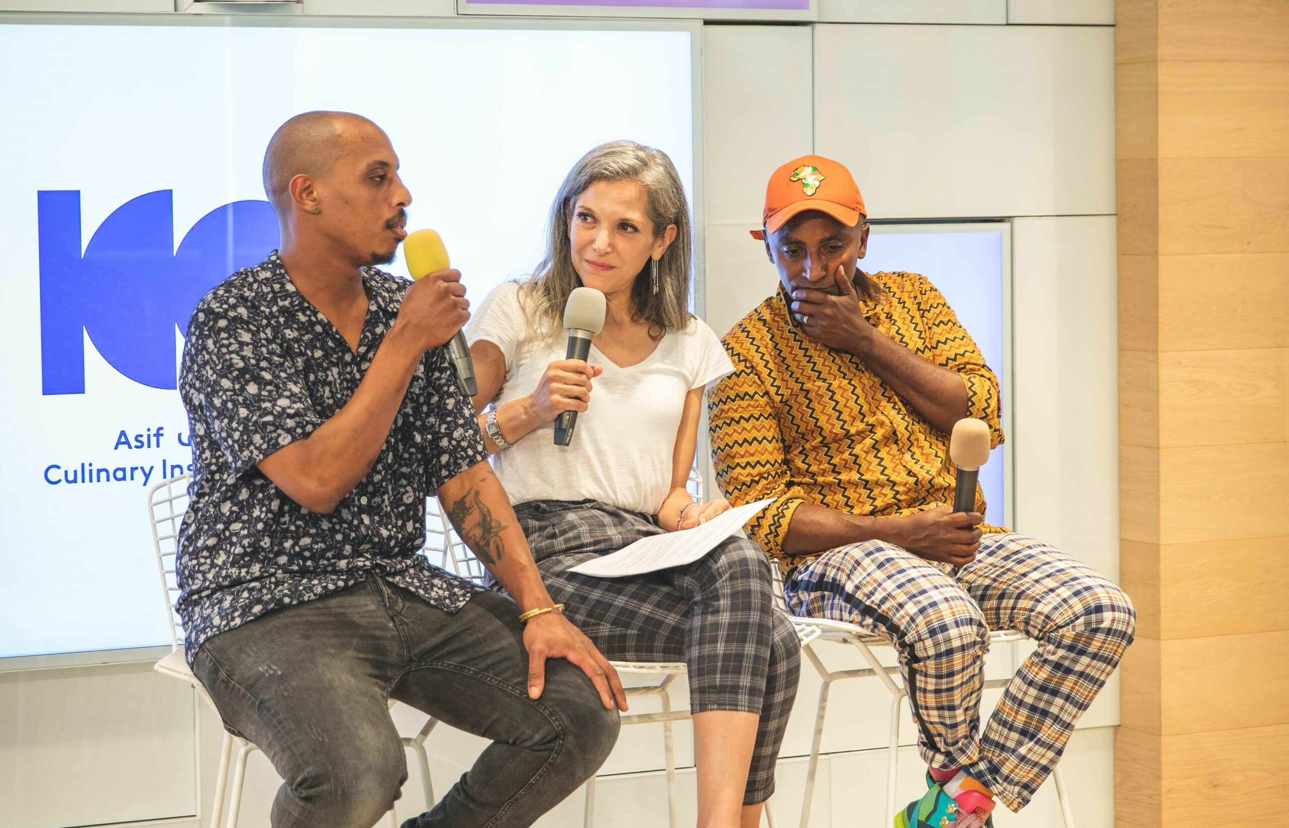 Chefs Marcus Samuelsson, Ruthie Russo, and Elazar Tamano sitting on stools, holding microphones