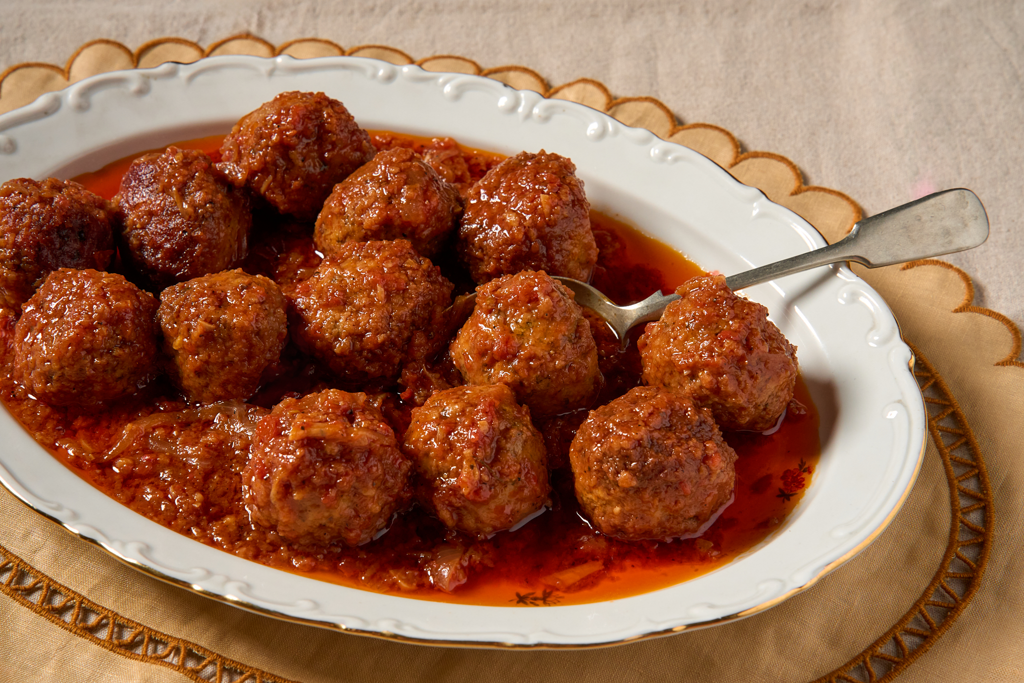 Red meatballs in sauce sit in a white oval-shaped plate