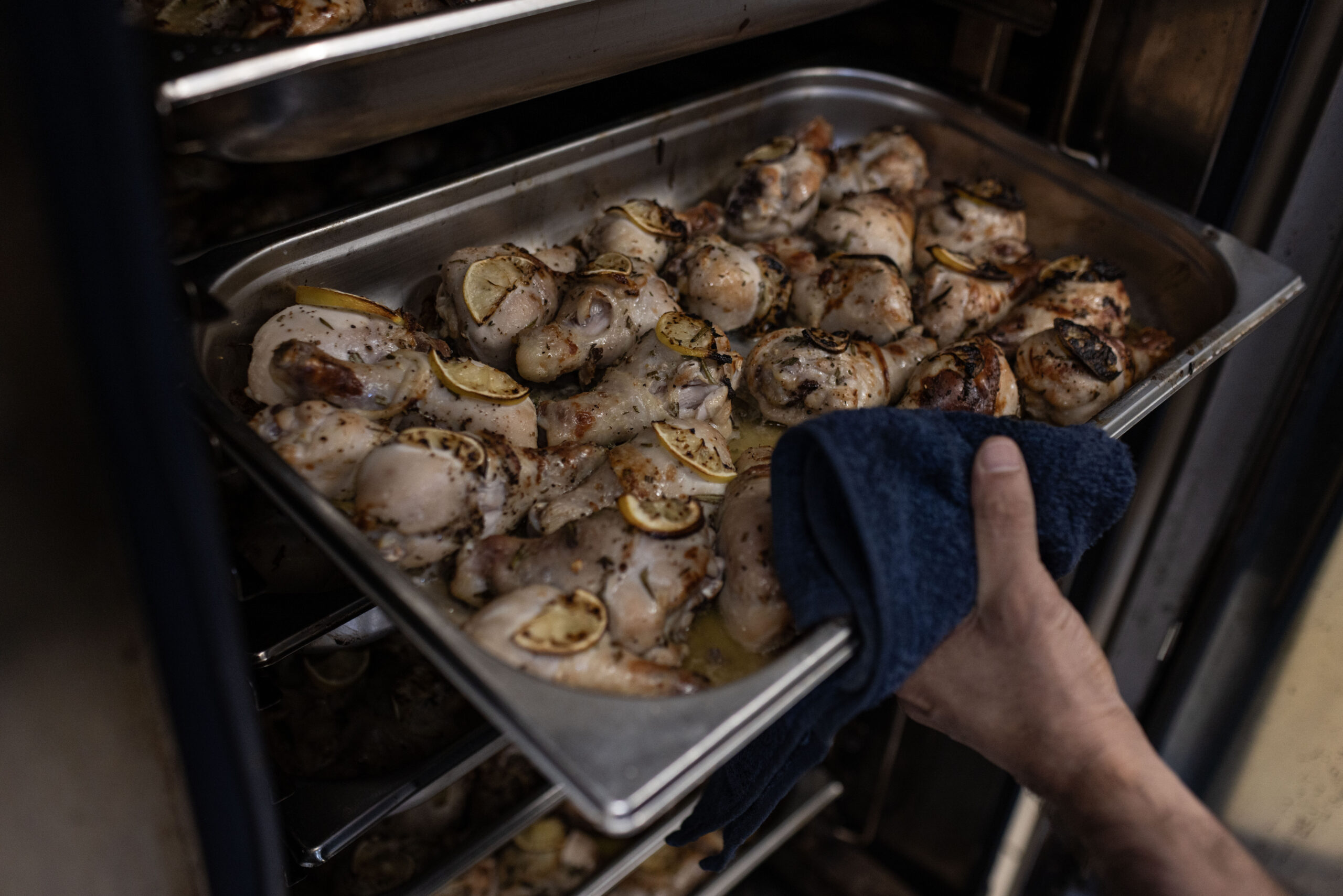 A hand holds a pan of chicken legs with lemon
