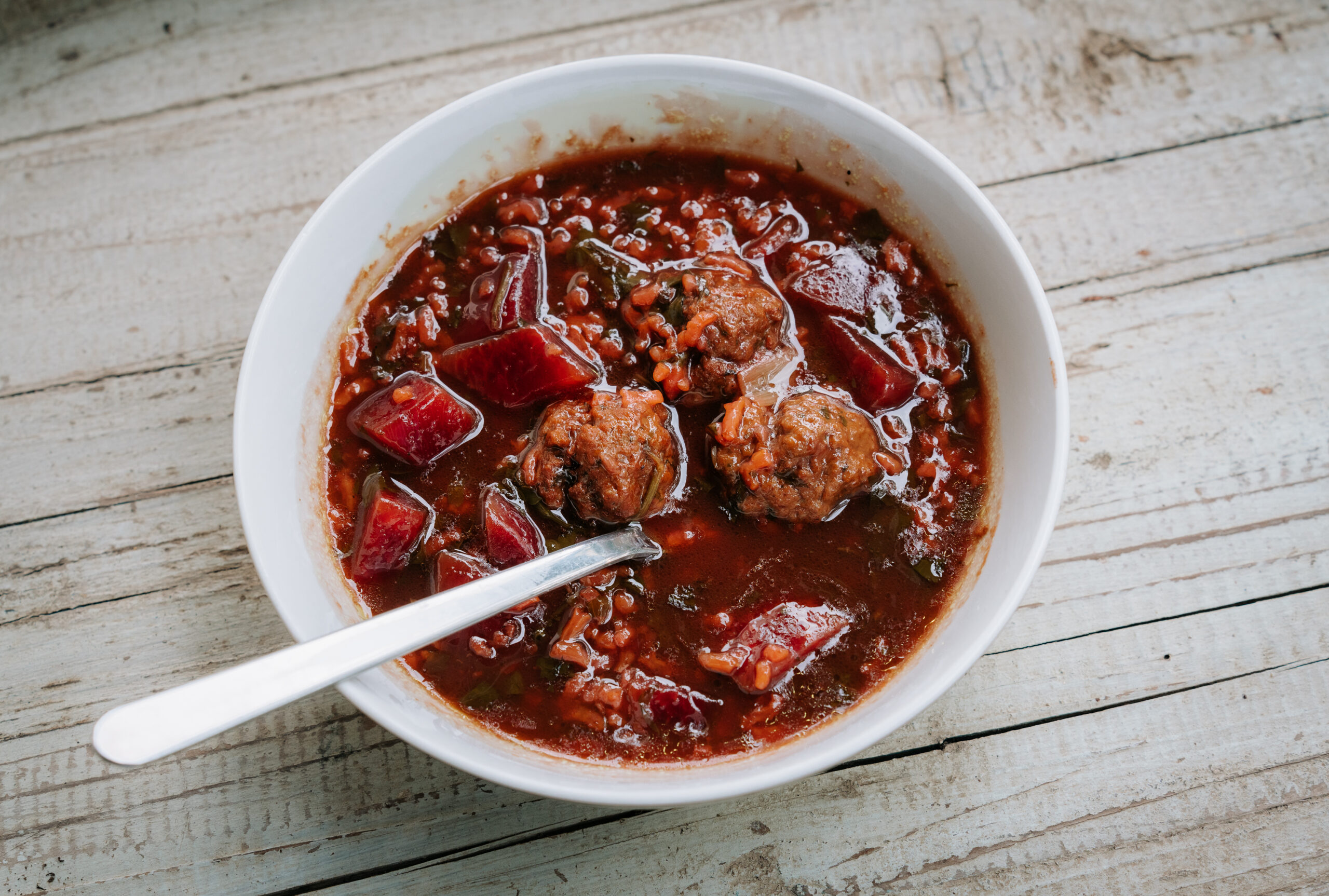 A white ceramic bowl of Persian beet and meatball stew