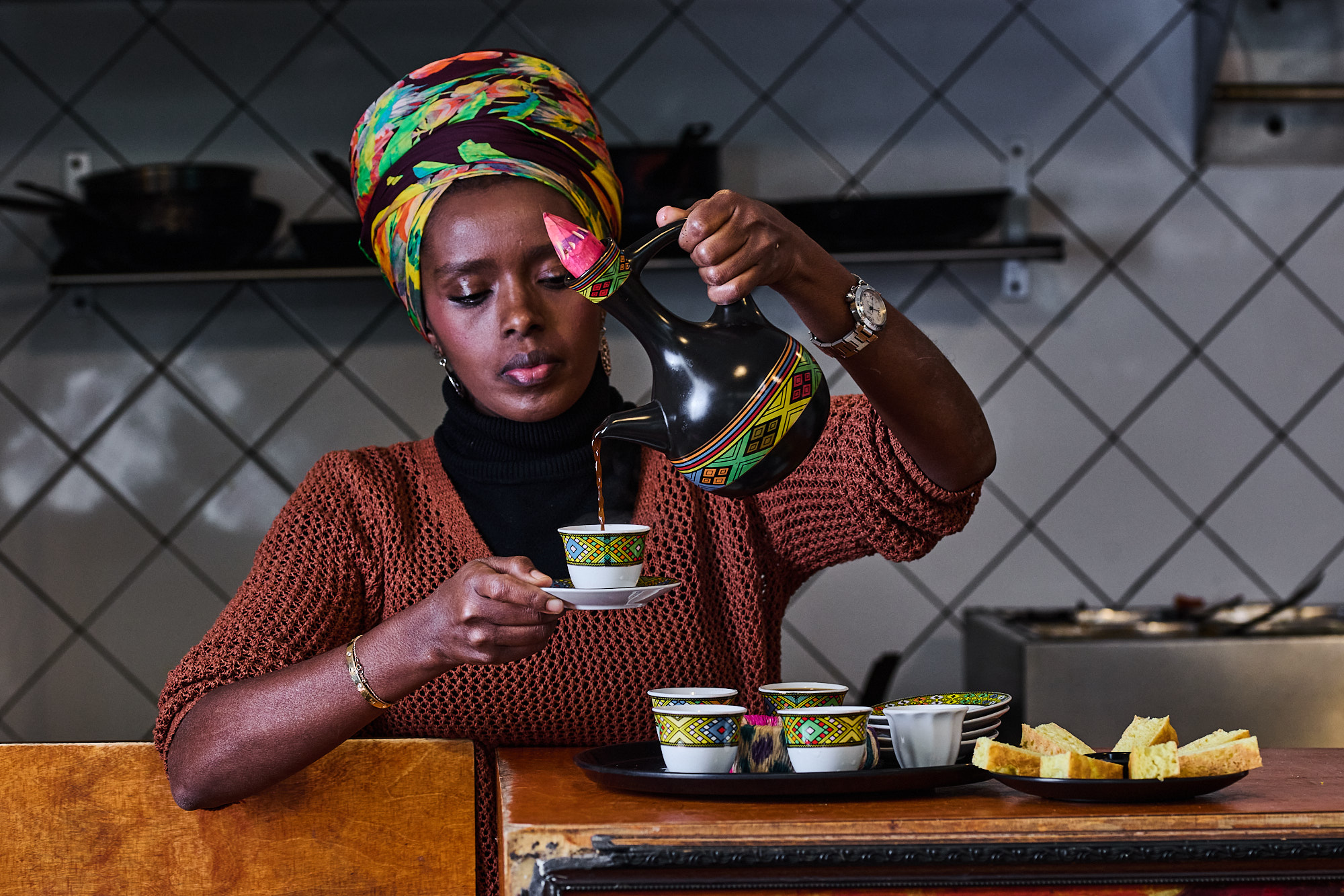 Ethiopian woman with head covering pouring coffee into small, colorful cups